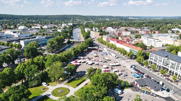 Ilmakuva kesäisestä kaupungista, jossa on viheralue, tori ja joki.