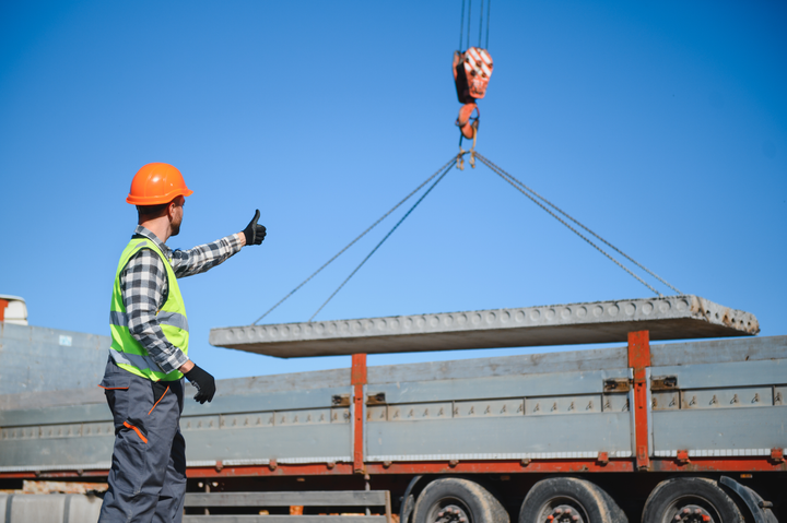 Nosurilla lasketaan rekan perävaunuun lastia. Perävaunun edessä työntekijä antaa käsimerkeillä ohjeita nosturin kuljettajalle.