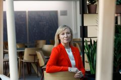 Katarina Murto istuu kuvan keskellä yllään punainen jakku. Taustalla pöytiä ja tuoleja.