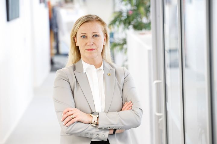 Katarina Murto keskellä kuvaa vaaleanharmaassa bleiserissä. Taustalla avokonttorin käytävä.