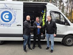 Kolme miestä seisoo pakettiauton edessä ja kättelevät.