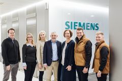 Ryhmäkuva seitsemästä henkilöstä seisomassa Siemens-logon edessä.