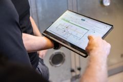 Kaksi ihmistä tarkastelee tablettia, jossa on talotekniikan järjestelmää kuvaava kaavio.