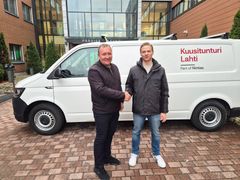 Kaksi miestä kättelee valkoisen pakettiauton edessä, taustalla tiilirakennus.