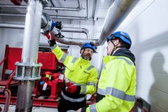 Kaksi henkilöä työskentelee teollisuuslaitoksen sprinklerijärjestelmän parissa käyttäen turvavarusteita.