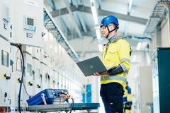 Mies työskentelee kannettavan tietokoneen kanssa sähkötekniikan parissa suojavarusteisiin pukeutuneena.