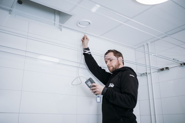 Mies tarkistaa ilmastointijärjestelmää sisätiloissa LVI-Trio-yrityksen työasussa.