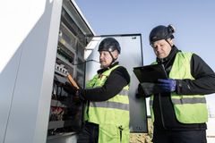 Kaksi huoltomiestä tarkastaa kylmälaitetta ulkona, yllään turvavarusteet ja huomioliivit.