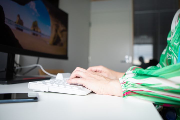Ihminen istuu tietokoneen ääressä kädet näppäimistöllä.