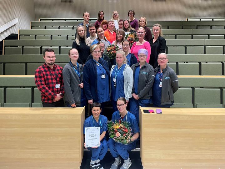 Joukko palkittuja henkilöitä katsoo kameraan hymyilee luentosalissa.