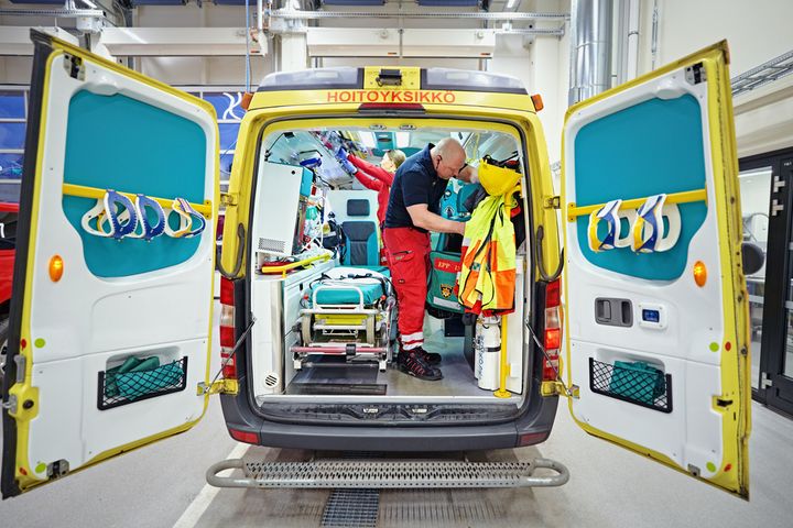 Ensihoitoauto, jossa takaovet auki ja sisällä hoitaja, joka tarkastelee varusteita.