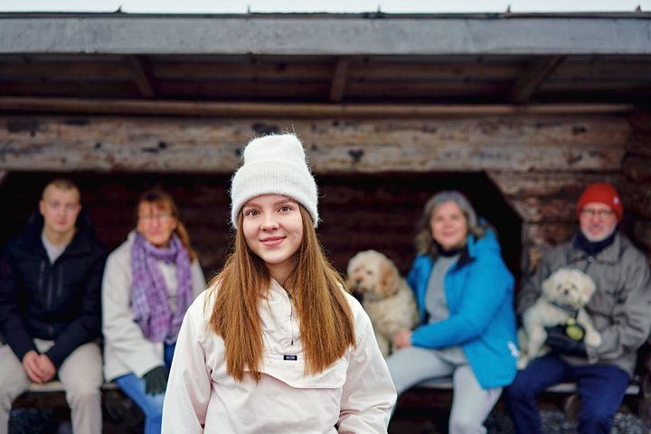 Nuori ihminen katsoo kameraan, taustalla enemmän henkilöitä sumeina.