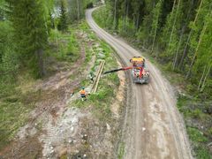 Ilmakuva: Kaksi asentajaa työskentelee tien varrella, varustaen puista pylvästä työryhmäauton avulla.