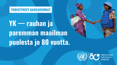 Pyöreiden 8 ja nolla kuvioiden keskellä rauhanturvaajanainen kättelee afrikkalaista äitiä, jolla on lapsi kantoliinassa. Teksti YK rauhan ja paremman maailman puolesta jo 80 vuotta.