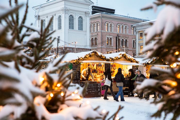 Kuvassa joulukuusi koristeineen ja valoineen etualalla. Takana näkyy Helsingin Senaatintorin rakennuksia sekä Tuomaan Markkinoiden kojuja jouluvaloineen.