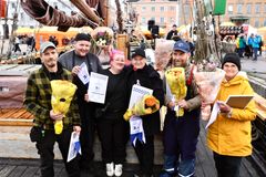 Voittajien poseeraus ulkona: kuusi henkilöä pitelee kukkakimppuja ja diplomeja tapahtumassa.