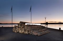 Asetelma tukkeja rannalla, yksi tukki on valaistu.