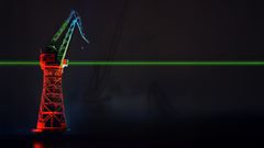 Värivalaistu nosturi, jonka yläosa on sininen ja alaosa punainen, yhdistyy vihreällä laserilla pimeässä.