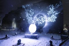 Valoteos Kansalaistorilla, jossa suuri, valkoinen, valaiseva muna ja koristeellisia valokuvioita heijastettuna pimeällä taustalla.