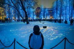 Henkilö katsoo lumista puistoa, jota valaisee värikäs valoteos. Puistossa on sininen valo.