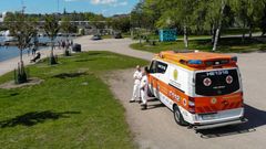 Ambulanssi pysäköitynä puistossa, taustalla näkyy rantaa ja puita.