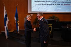 Pelastusjohtaja onnittelee henkilöä kättelyn aikana näyttämöllä, taustalla Suomen lippu ja esityskalvo.