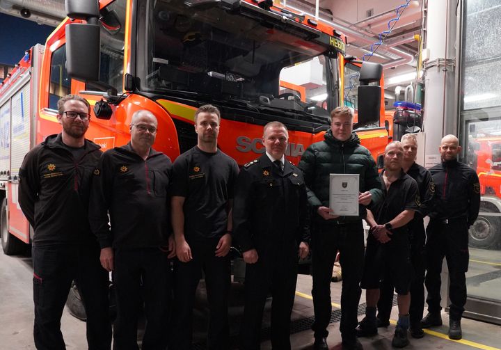 Palomiehet ja palkinnon saanut mies seisovat paloauton edessä