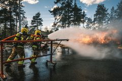 Kaksi palomiestä sammuttaa paloa vesiletkulla ulkona.