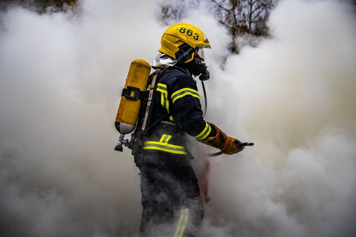 Palomies keltainen kypärä päässään työskentelee savussa.