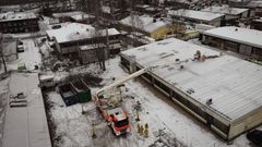 Ilmakuva nostolava-autosta talvisella piha-alueella, jossa työmiehet tekevät töitä rakennuksen katolla.