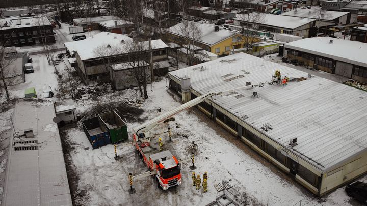 Ilmakuva nostolava-autosta talvisella piha-alueella, jossa työmiehet tekevät töitä rakennuksen katolla.