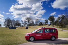 Punainen pelastuslaitoksen auto puistossa, taustalla puita ja pilvinen taivas.