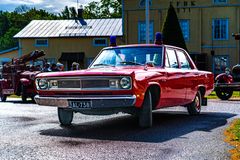 Punainen Plymouth Valiant 4D 100V vuodelta 1969, pysäköitynä ulkona historiallisessa ympäristössä, ympärillään vanhoja ajoneuvoja.