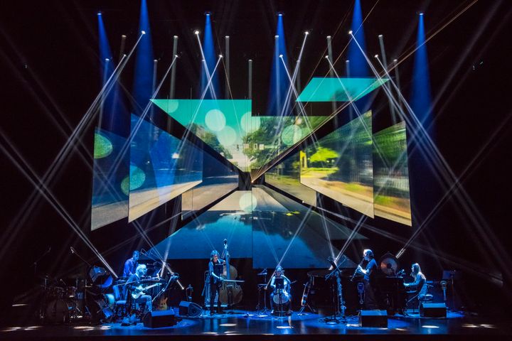 Konserttiesitys, jossa Bang on a Can All-Stars -orkesteri soittaa lavalla visuaalisesti vaikuttavien valotehosteiden ja projisointien ympäröimänä.