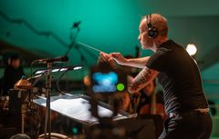 Mies johtamassa orkesteria kuulokkeet päässä.