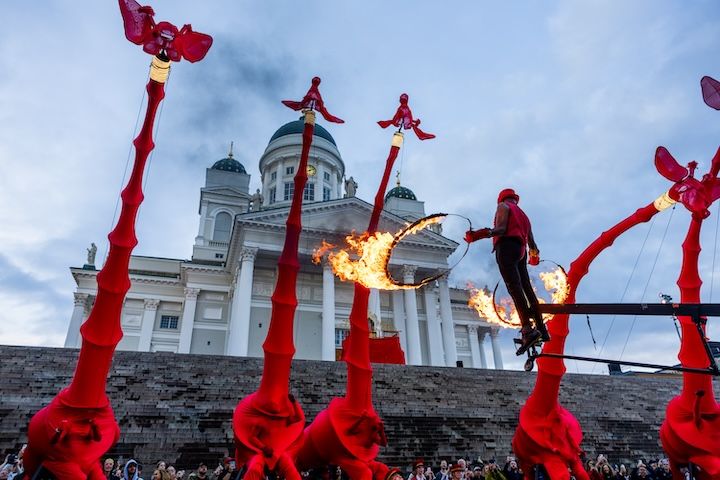 Kuvassa esiintyjä esittää eläinaiheista performanssia punaisessa asussa. Taustalla näkyy Helsingin Tuomiokirkko.