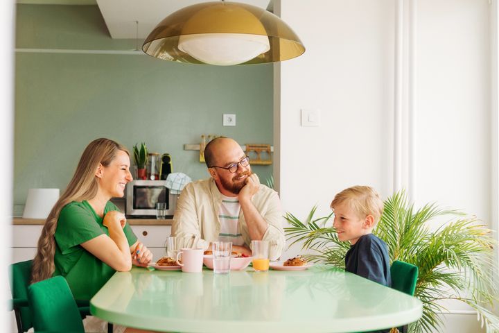Kuvassa kaksi aikuista ja leikki-ikäinen lapsi pöydän ääressä