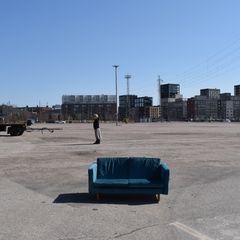 Sininen samettisohvat asfalttikentällä, taustalla kerrostaloja.