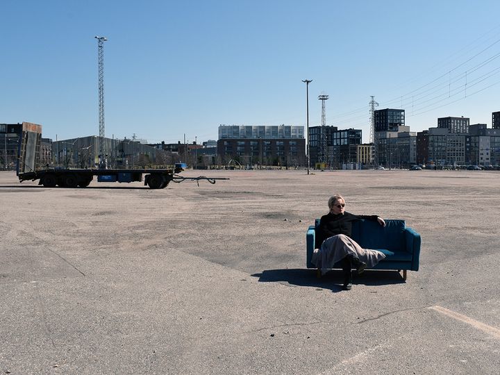 Pilvi Porkola istuu samettisohvalla keskellä parkkipaikkaa, takana näkyy kerrostaloja.