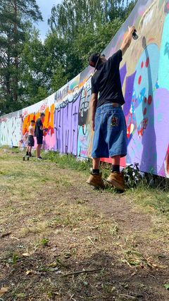 Nuoret tekevät taidetta graffitiseinällä.