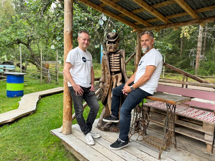 Teijo Monni ja Pertti Riikonen puisen veistoksen vieressä ulkona terassilla.