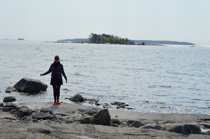 Henkilö seisoo kivisellä rannalla, taustalla on saari ja avomerta.