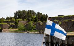 Suomenlippu liehuu etualalla, taustalla kivilinnoitus ja puita.