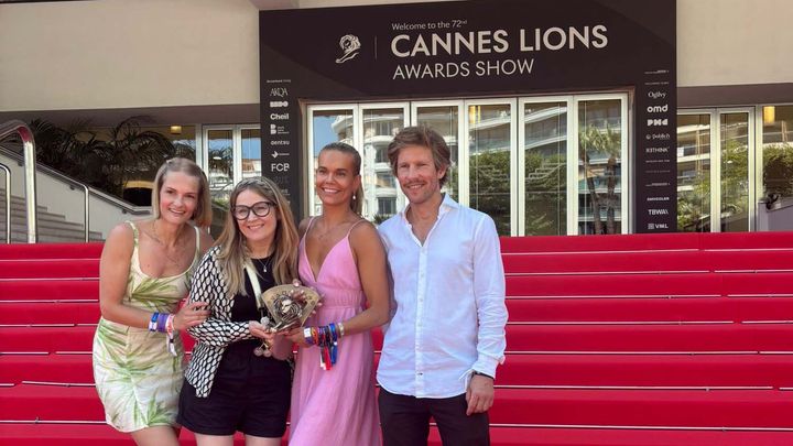 Neljä henkilöä seisoo punaisella matolla Cannes Lions -tapahtumassa, yksi heistä pitelee palkintoa.