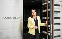 Susanna Niinistö-Sivuranta seisoo Haaga-Helia-kyltin vieressä ja pitää ovea auki. Hän hymyilee kameralle.