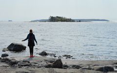Henkilö seisoo kalliorannalla, taustalla meri ja metsäinen saari.