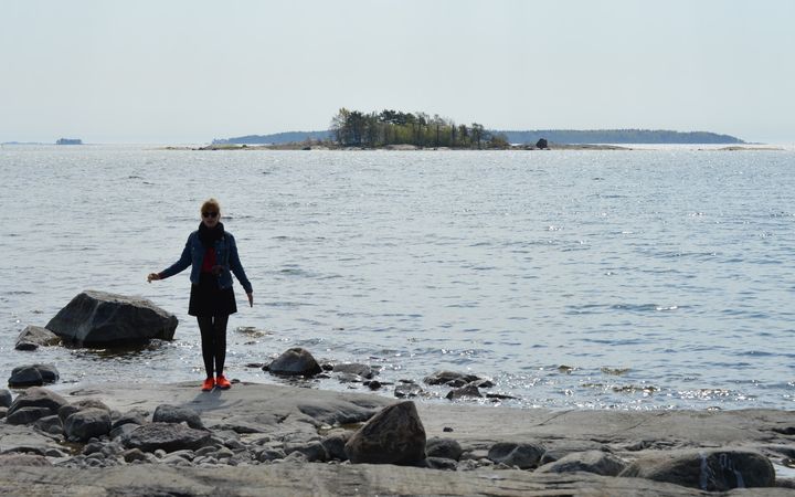 Henkilö seisoo kalliorannalla, taustalla meri ja metsäinen saari.