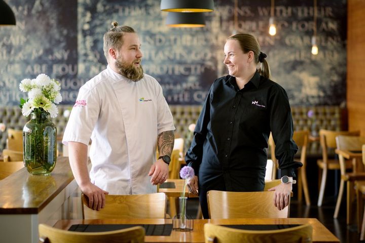 Kaksi henkilöä seisoo keskustellen ravintolassa.