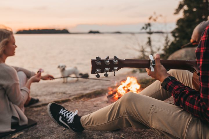 Henkilöt istuvat nuotion ääressä kalliolla meren rannalla kesäillan hämärtyessä, yksi soittaa kitaraa.