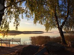 Järvimaisema auringonlaskussa, laituri etualalla ja puita ympärillä.